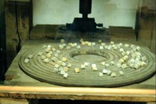 Märbelmühle: gusseiserne Platte mit Rillen, mit Würfeln bestückt