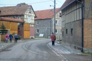 Dorfstraße mit Häusern; Schüler und Postfrau