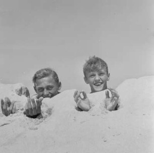 Zwei Jungs haben ihre Unterarme im Sand vergraben
