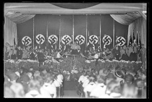 Musikkapelle in Uniform auf Bühne vor Publikum spielend (im Hintergrund mehrere Reichsbanner)