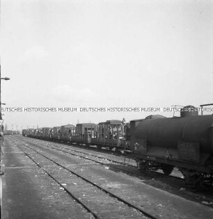 Fahrzeuge der Wehrmacht auf einem offenen Zug, im Vordergrund ein Zug der rumänischen C.F.R