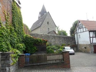 Treis an der Lumda-Evangelische Kirche - Ansicht von Westen mit Kirche (Spätromanische Gründung 13 Jh) über Kirchhofmauer (Wehrgang mit Steinbrüstung und Schießscharten abgetragen)