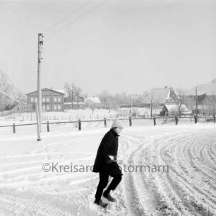 Rohlfshagener Weg / Dorfstraße: links Abzweigung des Klinkener Weges: dahinter Hinweisschild und Strommast: vorn Kind: im Hintergrund Zaun und Bauernhäuser: Winter