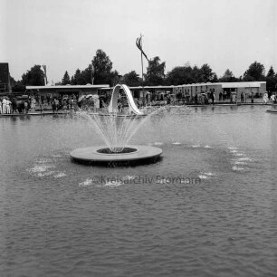 Sommerbad Tarpenbek: Am Hallenbad: Eröffnung: Nichtschwimmerbcken mit Springbrunnen (vorne) und Wasserrutsche, Gäste am Beckenrand, im Hintergrund Sanitäranlagen