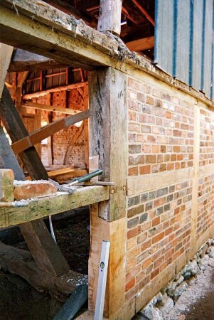 Dorfplatz (2): Fachwerkscheune: Sanierung: Teilansicht: Außenwand, Pfosten und Riegel nach teilweiser Erneuerung, vorne Gefache nach Entfernung von Ausmauerung, Blick in Innenraum, Werkzeug, oben Blechverkleidung: Juli 1994