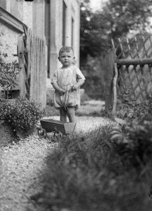 Kind mit Spielzeugwagen im Garten des Fotografen