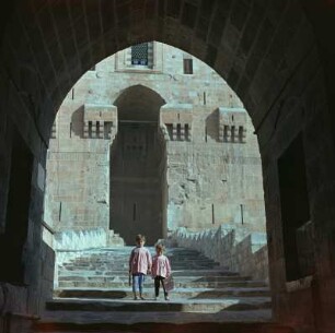 Blick durch einen Torbogen auf den Treppenaufgang zur Zitadelle von Aleppo, auf der Treppe zwei Kinder