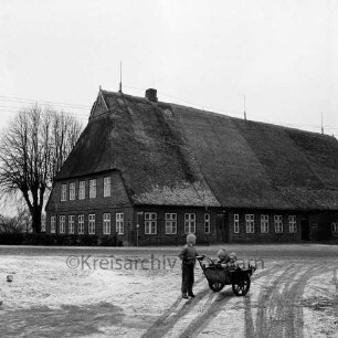 Gehöft Lienau: Reetdachhaus: vorn Kinder mit Schubkarre: hinten links Hecke und Bäume: Winter