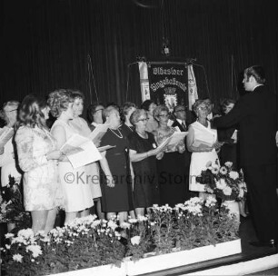 Oldesloer Singakademie von 1946: Oldesloer Hof: Saal: Festveranstaltung zum 25-jährigen Jubiläum: Gesangsvortrag des Chores: rechts Chorleiter: hinten Fahne: vorn Blumenschmuck: 26.09.1971