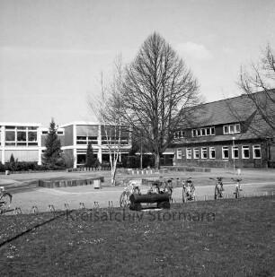 Grundschule: Hamburger Straße: ehemalige Volksschule: rechts Altbau: links Erweiterungsbauten: davor Schulhof mit Grünanlage und Baum: vorn Ständer mit Fahrrädern