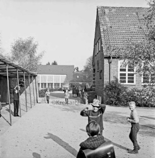 Volksschule: Soltausredder: vorn Schulhof mit Schulkindern: rechts Altbau mit Sträuchern: links Unterstand: hinten Turnhalle: davor Lieferwagen