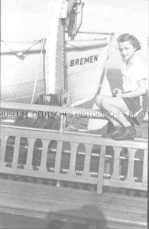 Junges Mädchen an Deck des Hochseepassagierdampfers "Bremen", vor einem Rettungsboot auf der Reling sitzend