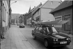 Gadebusch (Mecklenburg-Vorpommern) [Partnerstadt von Trittau]: Steinstraße: Autos, vorne Pkw mit Kanus auf Dach: rechts Einmündung von Schulstraße, Bildmitte Personen vor Eiscafé Roller: hinten Stadtkirche St. Jakob und St. Dionysius