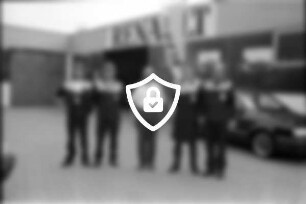 Renault-Autohaus Frenkler: Firmenhof: Werkstatt-Team, Gruppenfoto: Auszubildender [Name maskiert] Geselle [Name maskiert] Inhaber Kfz-Meister [Name maskiert] Kfz-Meister [Name maskiert] Geselle [Name maskiert] hinten Werkstatthalle, an Fassade Markenname, Werbeplakate Renault, Werbefahne, Pkw