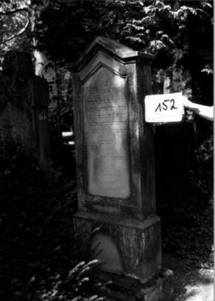 Grabstein 152 (Index: 100109764) Material: Sandstein Zustand: leicht verwittert Maße HxBxT: 197x64x24 cm Beschreibung: Stele, getreppter Sockel, giebelartiger Abschluß mit Verdachung, Schriftfeld eingetieft: Grabstein 152