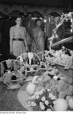Besucher betrachten Früchtekörbe und Weinflaschen der bulgarischen Sektion auf der Leipziger Herbstmesse 1954