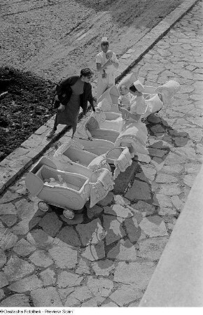 Pflegerinnen und Renate Rössing mit Kleinkindern im Kinderwagen vor dem Heimgebäude