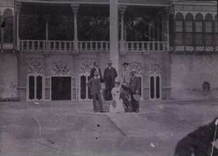 Gruppenportrait : Portraitaufnahme von einer Frau mit Kind und fünf Männern in einem Innenhof in Bagdad. Rechts vorne der Geograph Hugo Grothe (1869-1954).