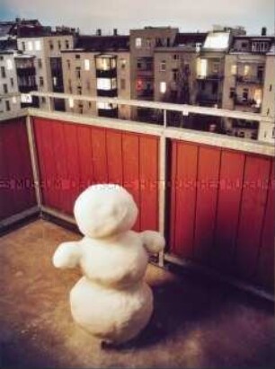 Schneemann auf einem Balkon, im Hintergrund Wohnhäuser (Altersgruppe 14-17)
