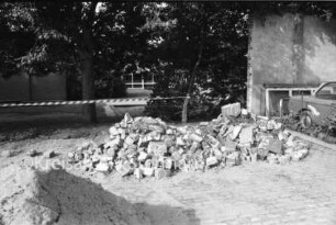 Matthias-Claudius-Schule [Grundschule]: Marktplatz: Schulhof: Schutthaufen mit Mauerresten und Sandhaufen: dahinter Absperrung, Bäume, Schulhof und Gebäude: rechts Zaun, parkender Pkw und Mauerstück