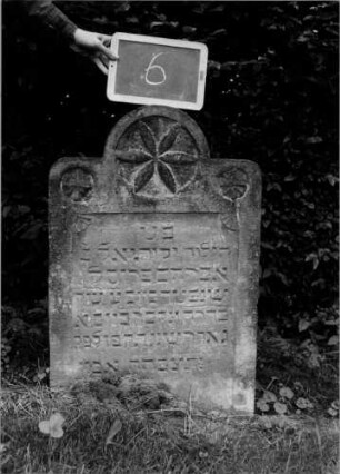 Grabstein 6 (Index: 100107142) Material: Sandstein Zustand: leicht verwittert Maße HxBxT: 83x55x9 cm Beschreibung: Stele, eingezogener Rundbogenabschluß Symbolik: secksblättrige Blüte im Rundbogen, seitlich je eine Blüte Besonderheit: Kindergrab: Grabstein 6