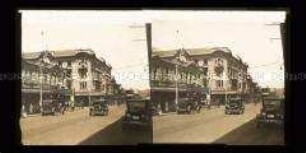 Geschäftsstraße mit Autos, Passanten und Läden