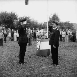 Meddewade: Freiwillige Feuerwehr Meddewade: Festplatz: Fahnenweihe: Kreisbrandmeister Heinz Poschmann und Wehrführer beim Salutieren: dahinter Mitte Rednerpult und Fahnenstange: hinten Zuschauer, Büsche, Bäume, Hausdach: 01.06.1974