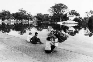 Hanoi. Erwachsene sitzen mit Kindern am Ufer eines Teiches
