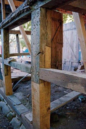 Dorfplatz (2): Fachwerkscheune: Sanierung: Detailaufnahme: Außenwand, Pfosten und Riegel teilweise nach Erneuerung, Schwellbalken auf Feldsteinfundament, Gefache nach Entfernung von Ausmauerung, Blick in Innenraum, hinten Scheunentor: Juli 1994