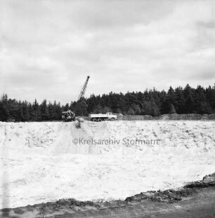 Oher Tannen: Kiesabbau: Blick in die Kiesgrube voller Sand: am gegenüberliegenden Rand in der Mitte Bagger beim Beladen eines Lkws: dahinter Tannenwald