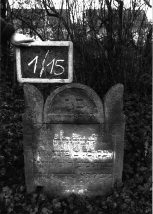 Grabstein 15 (Index: 99804873) Material: roter Sandstein Zustand: stark verwittert und eingesunken mit Textverlust Maße HxBxT: 170x54x10 cm Beschreibung: Stele, eingezogener Rundbogen, Eckakrotere: Grabstein 1/15