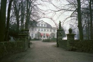Grönwohlhof: Herrenhaus: Eingangsfassade: mit mittigem Eingangsvorbau, Altan, großer Dreiecksgaube: Eckrisaliten: im Vordergrund Mauer, Einfahrtstor, Auffahrt