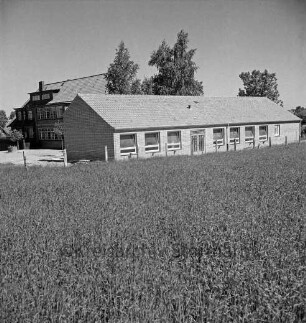 Volksschule: Schultwiete: Erweiterungsbau vor Fertigstellung: Außenansicht: davor Getreidefeld: links Baumaterial: hinten links altes Schulgebäude: dahinter Bäume
