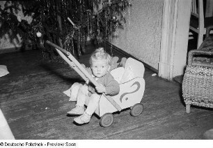 Porträt eines kleinen Mädchens mit Puppenwagen vor einem Weihnachtsbaum