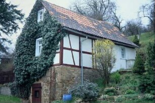Häuschen mit Steinsockel, Fachwerk-OG, berankter Fassade am Hang