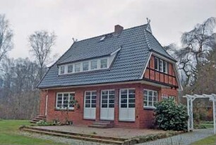 Am Rehm 52: giebelständiges Backsteinhaus: rechts Straßenfront, Giebel mit Vorkragung und Fachwerk, oben Giebelzier Pferdeköpfe: um Gebäudeecke Auslucht mit Terrassentür: westliche Traufseite, breite Flachgaube, Terrasse: Gartenweg, Pergola