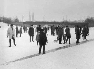 Hamburg. Die zugefrorene und verschneite Außenalster im Winter 1962. Menschen bestaunen das Ereignis. Manch einer nutzt das Eis zu einer kleinen Rutschpartie. Im Hintergrund die Kennedy- und Lombardsbrücke sowie die Silhouette der Altstadt