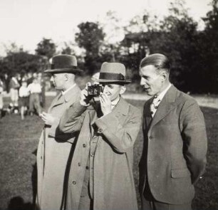 Gruppe von Zuschauern am Rande eines Fußballfeldes (der mittlere mit Fotoapparat)