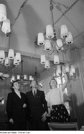Drei Personen bei der Begutachtung von Deckenlampen auf der Leipziger Herbstmesse 1954