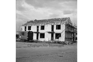 Kolberg-Körlin-Straße: Mehrfamilienhaus im Rohbau mit Gerüst und Dachsparren: davor Baumaterial: links Bauwagen: hinten rechts weiteres Haus im Bau