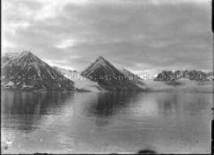 Dunkle Bergreihe mit Schneefurchen, Gletscher, Steilküste und spiegelglattem Fjord, Nordlandreise, Norwegen