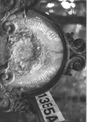 Grabstein 1365 (Index: 99900291) Material: Sandstein Zustand: stark verwittert Maße HxBxT: 168x60x25 cm Beschreibung: aufgesockelte Stele mit eingezogenem Rundbogenabschluss, Giebel- und Eckakroterien mit Voluten, im Bogenfeld Kranz, darunter Ranken mit Voluten, Blüten und Blättern Symbolik: Kranz, Voluten, Blätter, Blüten: Grabstein 1365A