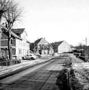 Dorfstraße mit Kopfsteinpflaster: links Gasthof Schwarzenbeck: davor Baum und Pkws: hinten Bauernhäuser: rechts Vorgarten mit Mauer: Winter