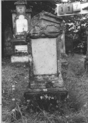 Grabstein 117 (Index: 99800084) Material: Sandstein Zustand: verwittert, linke Seite abgeschlagen, Originalschriftplatte fehlt Maße HxBxT: 124x47x21 cm Beschreibung: Stele, Giebelabschluß mit Verdachung, rechteckige unbeschriebene Ersatzplatte eingelassen, getreppter Sockel: Grabstein 117