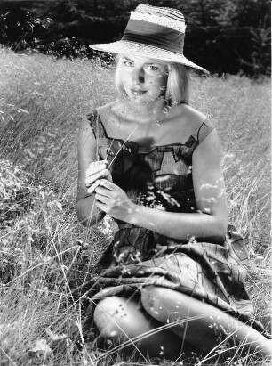 Ein unbekanntes Fotomodel sitzt auf einer Wiese. Sie hält Gras in ihren Händen. Aufgenommen 1961