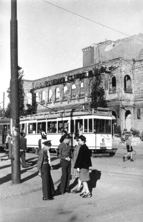 Berlin. Straßenbahn der Linie 77 (Triebwagen 5955) in einem Haltestellenbereich. Ansicht mit Wartenden. Blick gegen Ruine