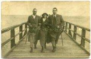Eine Frau mit zwei Männern auf einer Seebrücke