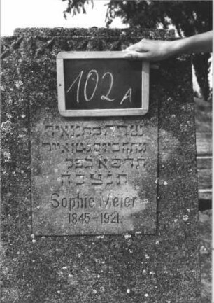 Grabstein 102 (Index: 100114113) Material: Kalkstein Zustand: leicht verwittert Maße HxBxT: 145x57x20 cm Beschreibung: konische Stele, flacher Abschluß, Schriftplatte rechteckig Symbolik: vierzackiges Sternenfries: Grabstein 102A