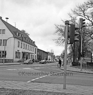 Am Markt / B 75: vorne Kreuzung, nach rechts Abzweig Rathausstraße, nach links Abzweig Straße Wurth: neue Ampelanlage: Fahrradfahrer wartet am Fußgängerübergang: Wegweiser nach Lübeck: links Postgebäude
