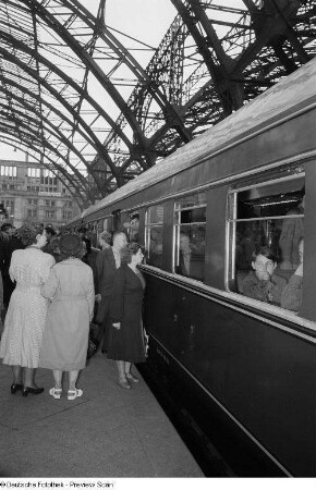 Reisende auf dem Bahnsteig vor einem Eisenbahnwagen